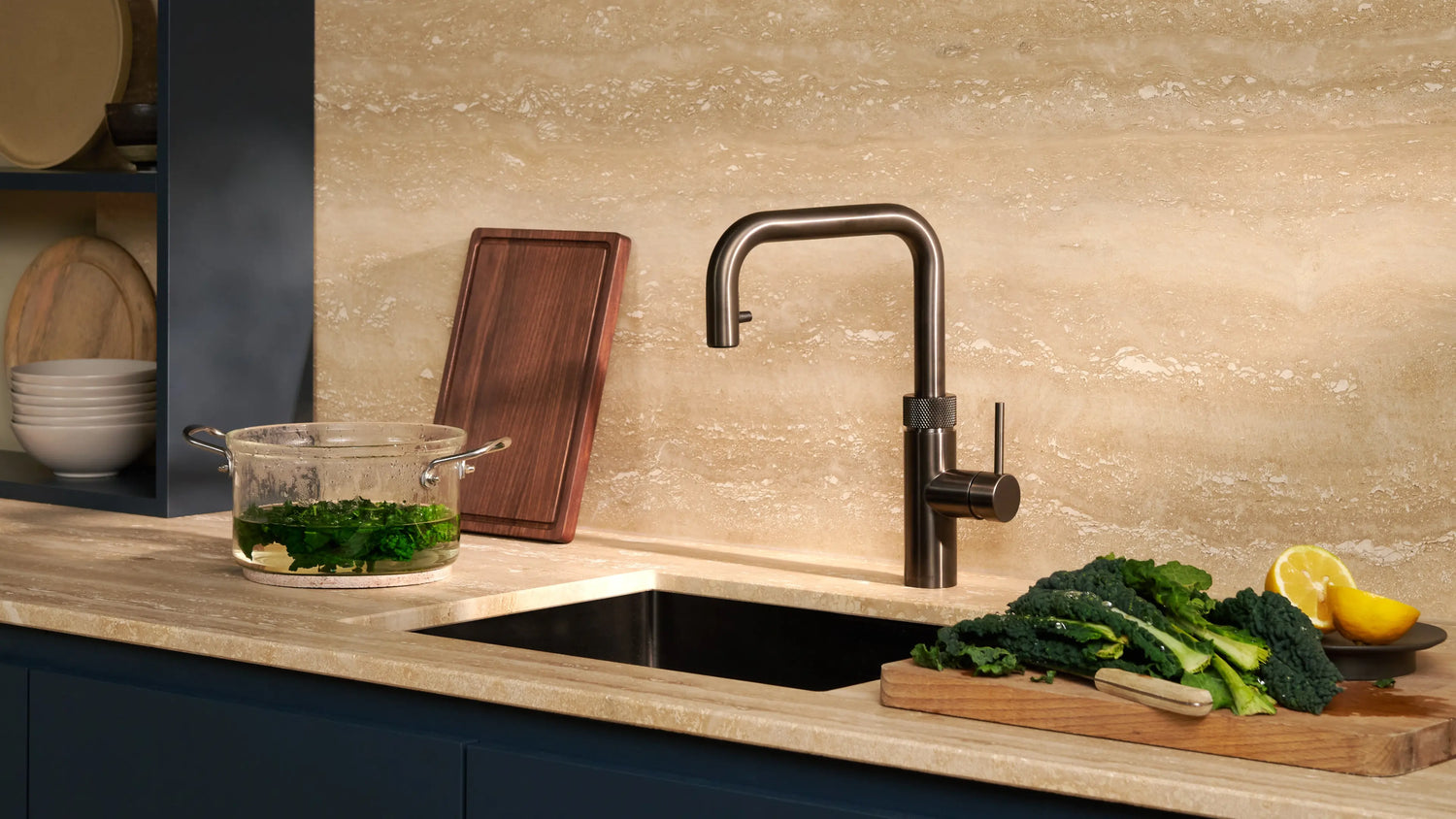 Quooker Flex Square gunmetal boiling water tap installed in a modern kitchen with marble countertop, vegetables, and a glass pot beside the sink, available at Spoelbakhuis.