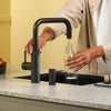 Person using the Quooker Flex Square black boiling water tap to fill a glass bottle in a modern kitchen, available at Spoelbakhuis.
